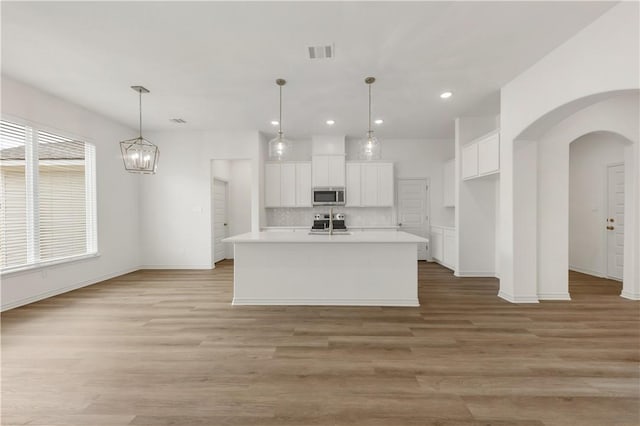 kitchen with decorative light fixtures, appliances with stainless steel finishes, a kitchen island with sink, decorative backsplash, and white cabinets