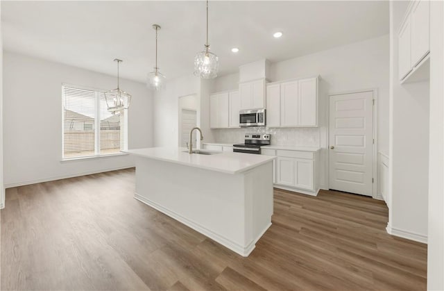 kitchen featuring sink, white cabinetry, decorative light fixtures, stainless steel appliances, and a kitchen island with sink