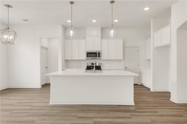 kitchen featuring appliances with stainless steel finishes, pendant lighting, sink, white cabinets, and a center island with sink