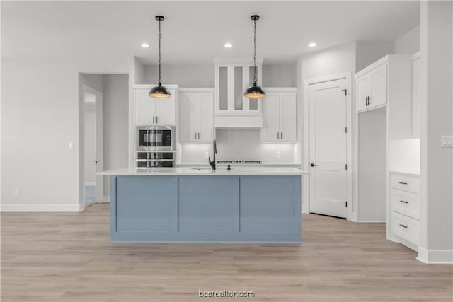 kitchen with decorative light fixtures, light hardwood / wood-style floors, white cabinetry, and an island with sink