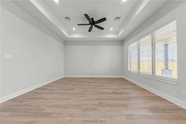 unfurnished room featuring a raised ceiling, ceiling fan, and light hardwood / wood-style floors