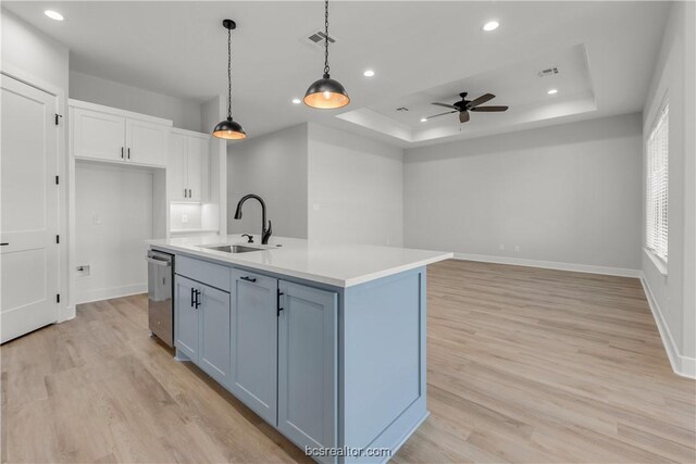 kitchen featuring stainless steel dishwasher, a raised ceiling, sink, hanging light fixtures, and an island with sink