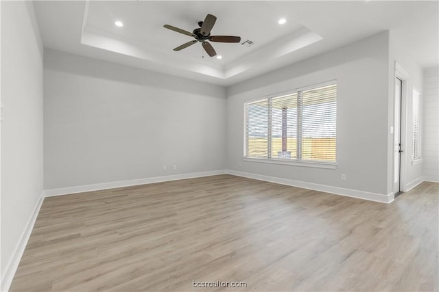 empty room featuring light wood-type flooring, a tray ceiling, and ceiling fan