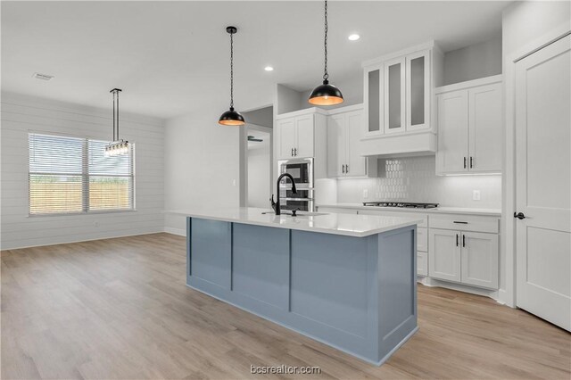 kitchen featuring a kitchen island with sink, sink, white cabinets, and hanging light fixtures