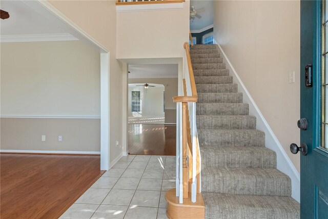 stairway with ceiling fan, wood-type flooring, and crown molding