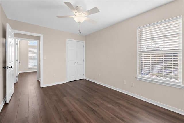 unfurnished bedroom featuring ceiling fan, a closet, dark wood-type flooring, and multiple windows