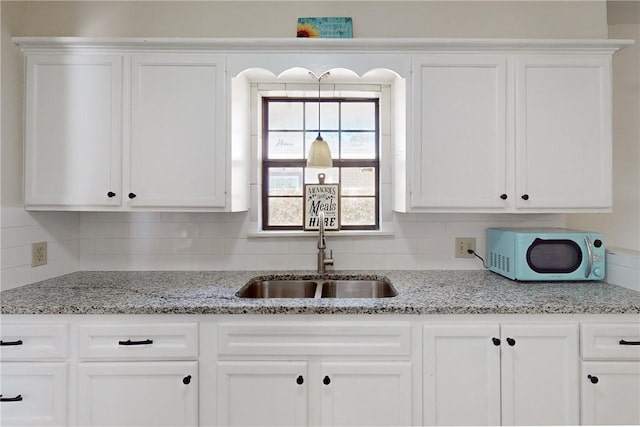 kitchen with tasteful backsplash, white cabinetry, sink, and light stone counters