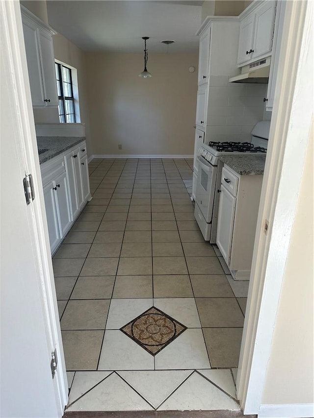 kitchen with light tile patterned floors, gas range gas stove, hanging light fixtures, backsplash, and white cabinets