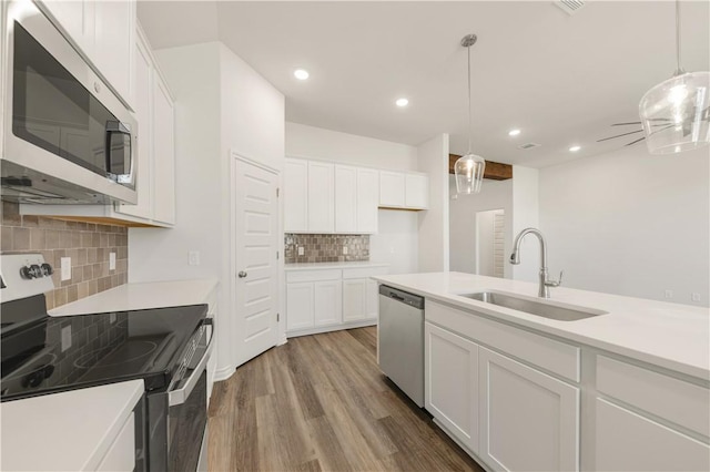 kitchen featuring white cabinetry, sink, stainless steel appliances, decorative light fixtures, and hardwood / wood-style flooring