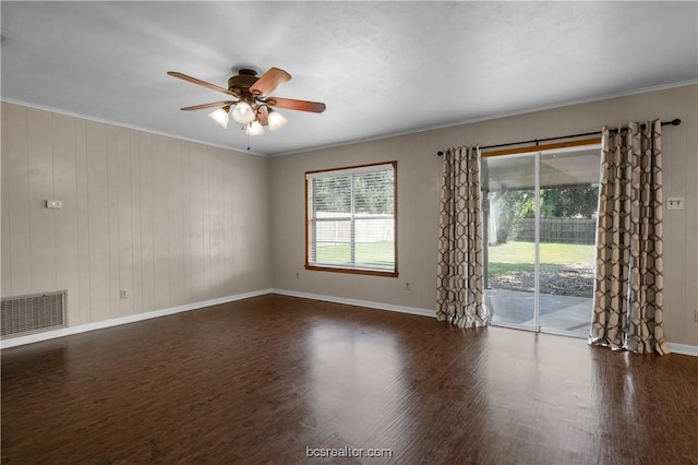 empty room with dark hardwood / wood-style floors, ceiling fan, crown molding, and wooden walls