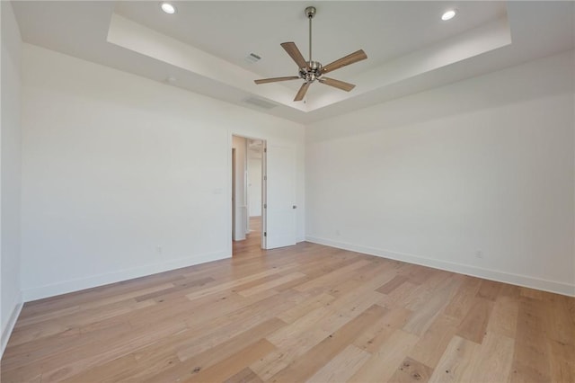 unfurnished room with light hardwood / wood-style flooring, ceiling fan, and a tray ceiling