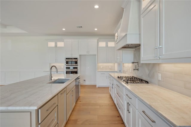 kitchen with sink, appliances with stainless steel finishes, premium range hood, light hardwood / wood-style floors, and white cabinets