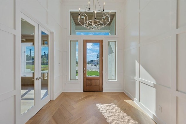 entrance foyer with an inviting chandelier, french doors, and light parquet floors