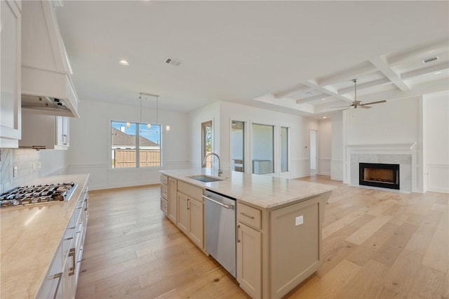 kitchen with sink, stainless steel appliances, light stone counters, an island with sink, and custom range hood