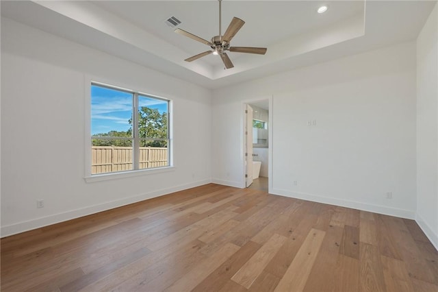 empty room with ceiling fan, light wood-type flooring, and a tray ceiling