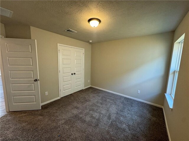 unfurnished bedroom with a closet, a textured ceiling, and dark colored carpet