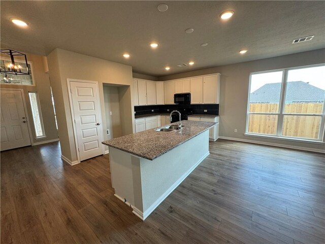 kitchen with stone counters, white cabinetry, dark hardwood / wood-style flooring, and a kitchen island with sink