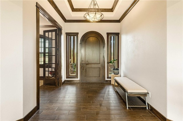 entryway with crown molding, a tray ceiling, arched walkways, baseboards, and wood finished floors