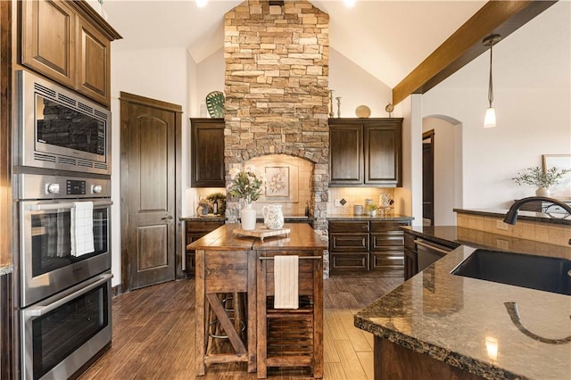 kitchen with a sink, stainless steel appliances, backsplash, arched walkways, and dark wood finished floors