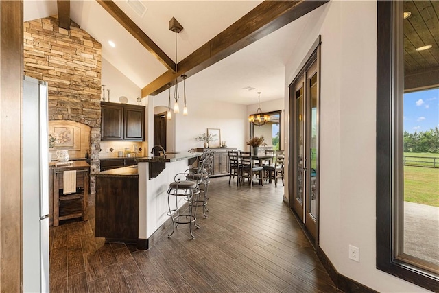 kitchen with a kitchen breakfast bar, dark countertops, beam ceiling, dark wood-style flooring, and a notable chandelier