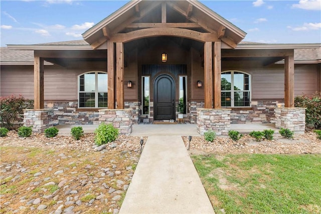 property entrance featuring covered porch, roof with shingles, and stone siding