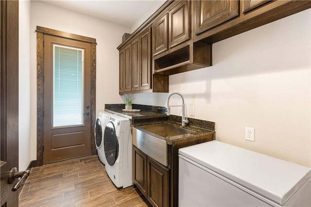 clothes washing area with a sink, cabinet space, washing machine and clothes dryer, and light wood-style flooring