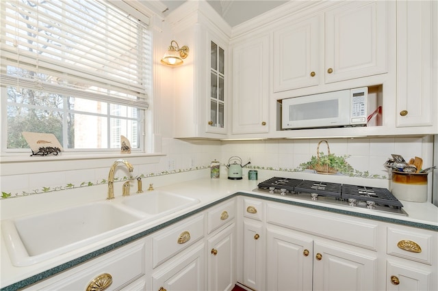 kitchen with white microwave, white cabinetry, stainless steel gas cooktop, and a sink