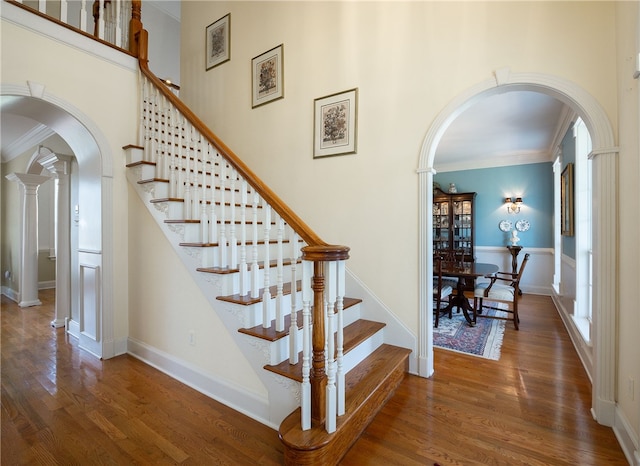 stairway featuring a towering ceiling, arched walkways, wood finished floors, and ornamental molding