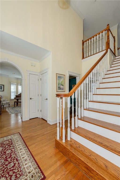 foyer featuring stairs, arched walkways, wood finished floors, and ornamental molding