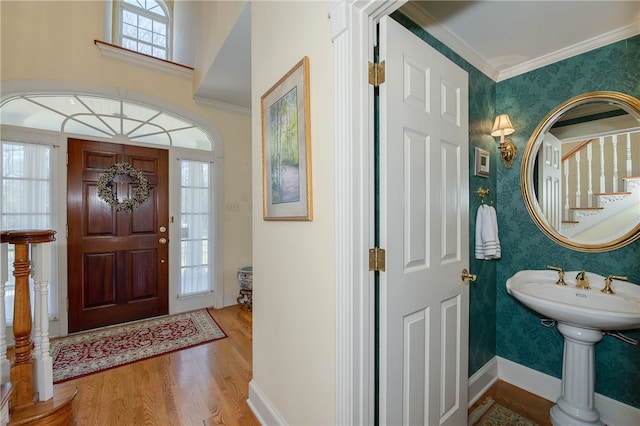 entrance foyer with wallpapered walls, ornamental molding, wood finished floors, baseboards, and stairs