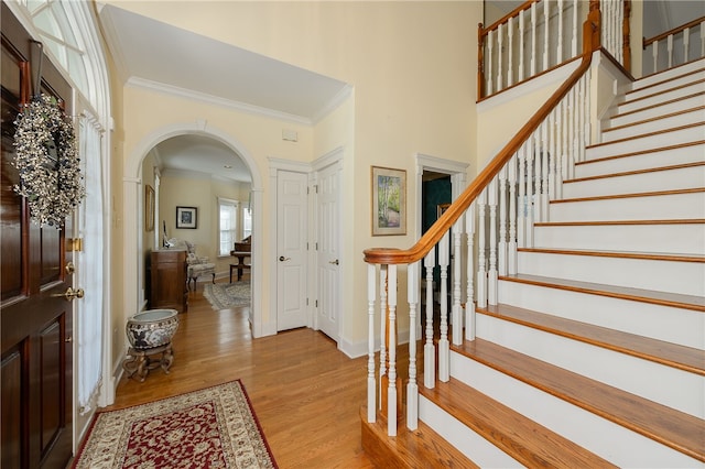 entryway with baseboards, arched walkways, stairway, wood finished floors, and crown molding