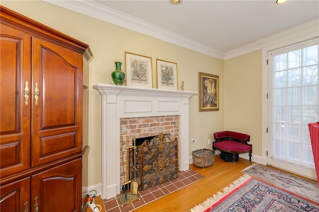 living area with a brick fireplace, crown molding, baseboards, and wood finished floors