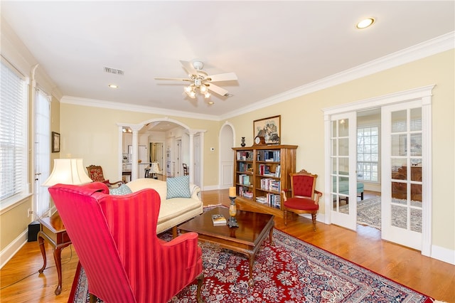 living room featuring arched walkways, wood finished floors, visible vents, ornate columns, and crown molding