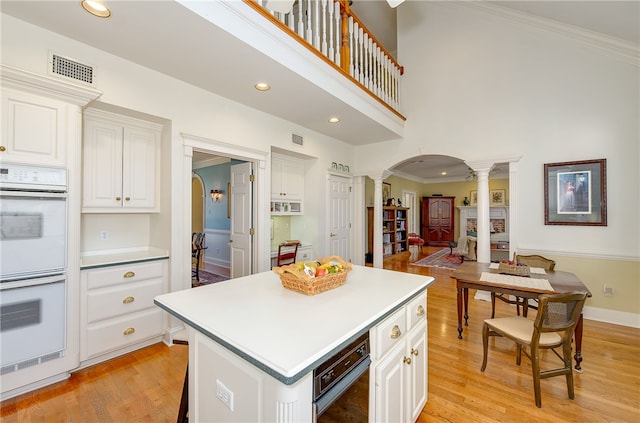 kitchen featuring arched walkways, white double oven, visible vents, light wood-type flooring, and decorative columns