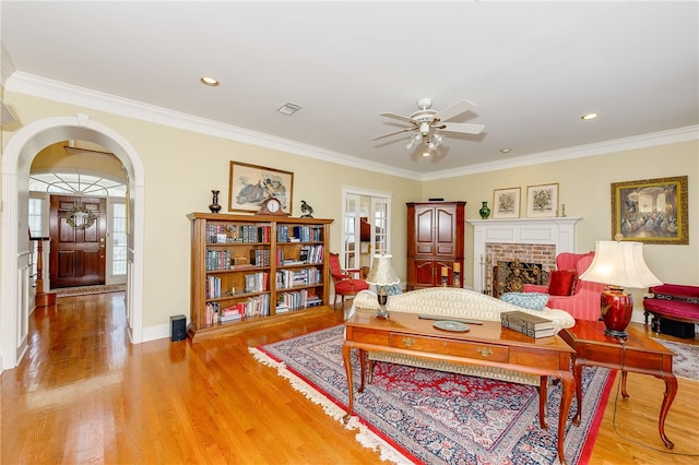 living area featuring a brick fireplace, light wood-style flooring, visible vents, and arched walkways