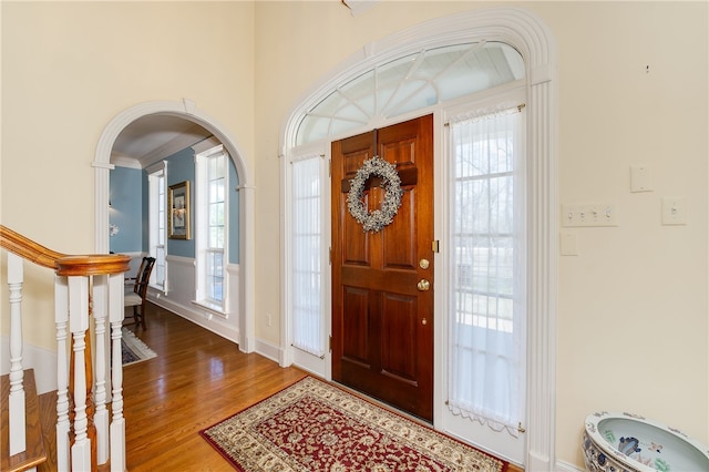 entrance foyer featuring arched walkways, stairway, and wood finished floors