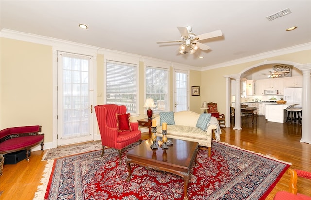 living room with arched walkways, visible vents, a ceiling fan, ornate columns, and crown molding