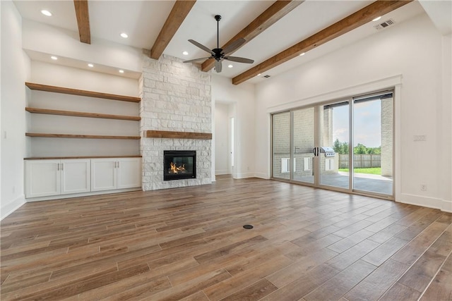 unfurnished living room with beam ceiling, hardwood / wood-style flooring, a stone fireplace, and ceiling fan