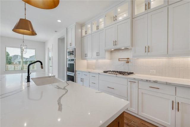 kitchen with sink, appliances with stainless steel finishes, pendant lighting, light stone countertops, and white cabinets