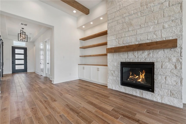 unfurnished living room with beam ceiling, a large fireplace, and light wood-type flooring