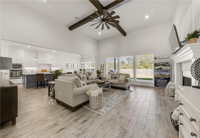 living room with beam ceiling, ceiling fan, high vaulted ceiling, and light wood-type flooring