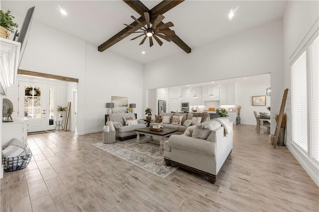 living room featuring beamed ceiling, a high ceiling, light hardwood / wood-style floors, and ceiling fan