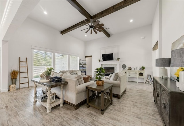 living room with beamed ceiling, ceiling fan, light hardwood / wood-style floors, and a towering ceiling