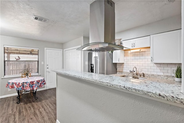 kitchen with island range hood, high end refrigerator, a sink, visible vents, and white cabinets