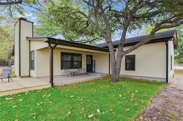 rear view of property with a chimney, a lawn, a patio area, and stucco siding