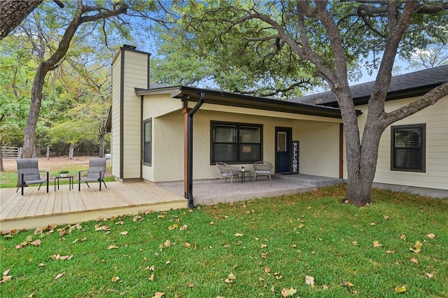 back of house featuring a yard, a chimney, stucco siding, fence, and a wooden deck