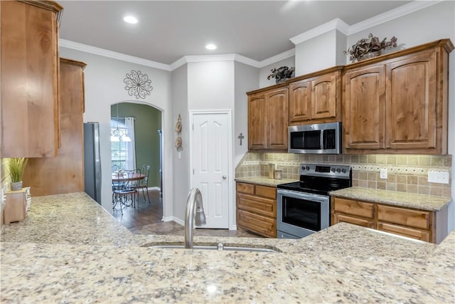 6997 Shirley Rd, Bryan, TX 77808 - kitchen with stainless steel appliances, arched walkways, backsplash, brown cabinetry, and crown molding