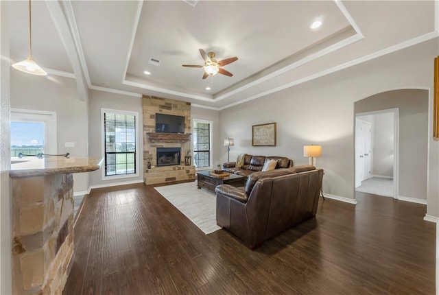 6997 Shirley Rd, Bryan, TX 77808 - living area featuring a tray ceiling, a stone fireplace, a ceiling fan, dark wood-style floors, and arched walkways