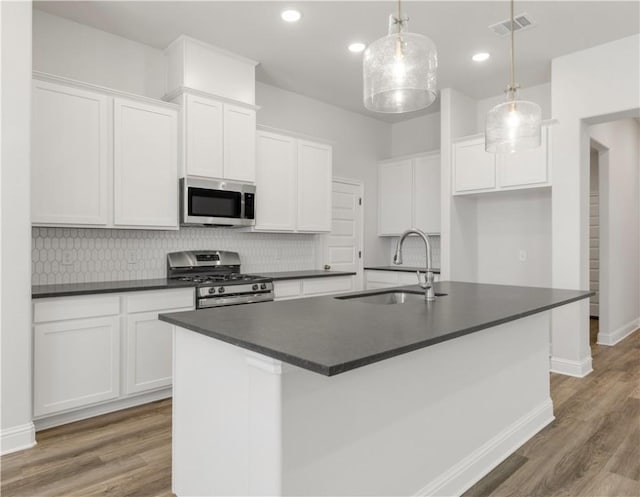 kitchen featuring dark countertops, a sink, appliances with stainless steel finishes, white cabinets, and a kitchen island with sink