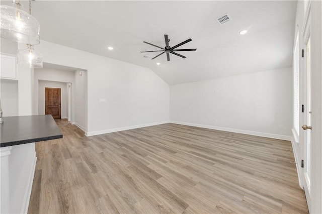 unfurnished living room featuring light wood-type flooring, visible vents, lofted ceiling, and baseboards